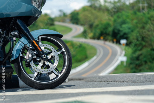 Motorcycle with sleek design is parked on road with winding path in background, surrounded by lush greenery