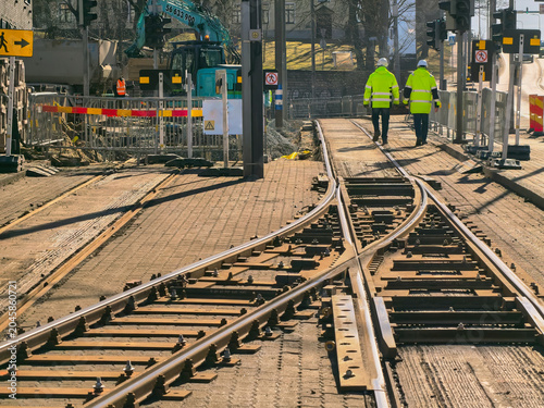 Fotografie A rear view of two road workers in hard hats and bright yellow overalls walking along a section of tram line under construction