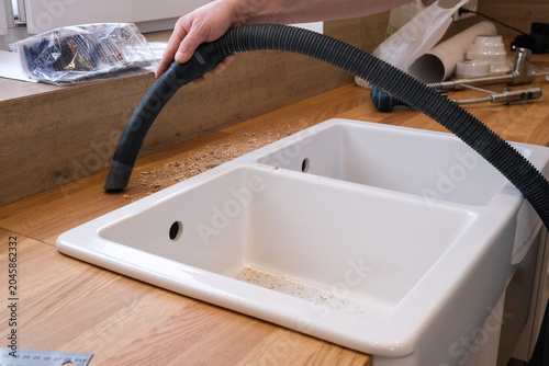 Hands vacuuming wood countertop around a white double kitchen sink