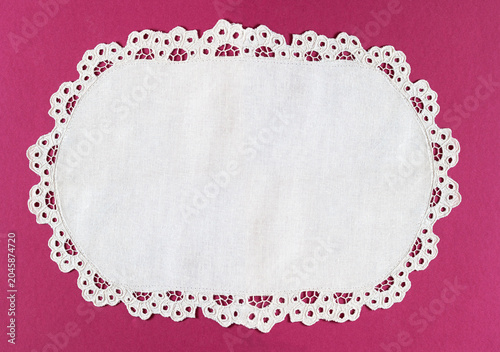 Oval white handmade table napkin with cutwork embroidered lace edge on a pink background. Blank space for text. Close-up, top view, copy space, flat lay, mock up