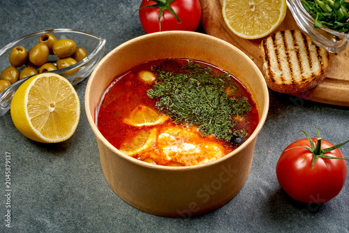 Photos Traditional red hodgepodge solyanka soup with lemon, olives and fresh dill in cr