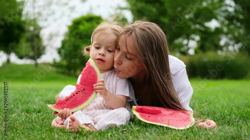 mother and daughter eating watermelon in a park, mother and child lying on a green lawn in summer