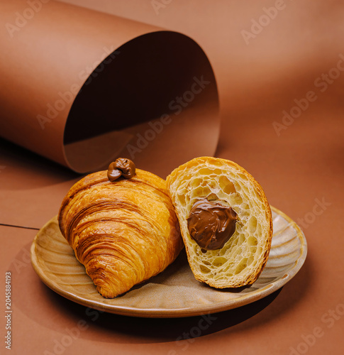 Fresh croissant with chocolate filling on a simple brown plate