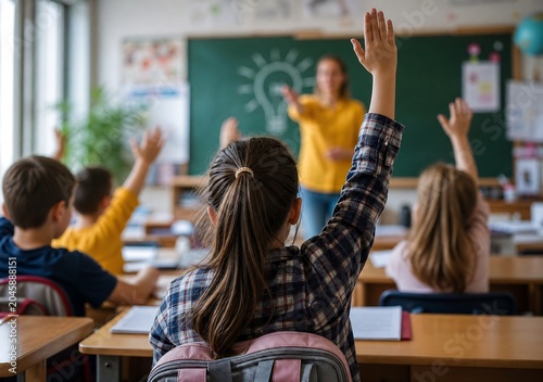 Enthusiastic elementary school students raising hands in classroom to answer question during lesson with teacher