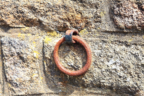 Canvastavla Ein stark verrosteter, runder Eisenring ist fest in einer alten Natursteinmauer in Locronan verankert und zeugt als historisches Detail von vergangenen Zeiten