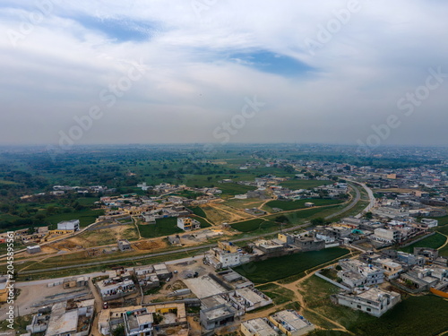 Aerial view of residential houses and green agricultural fields under a cloudy sky near the outskirts of the city Islamabad, Islamabad Capital Territory, Pakistan.