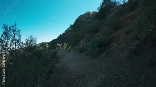 Woman hiking on a mountain trail through scrubby hills under a clear blue sky