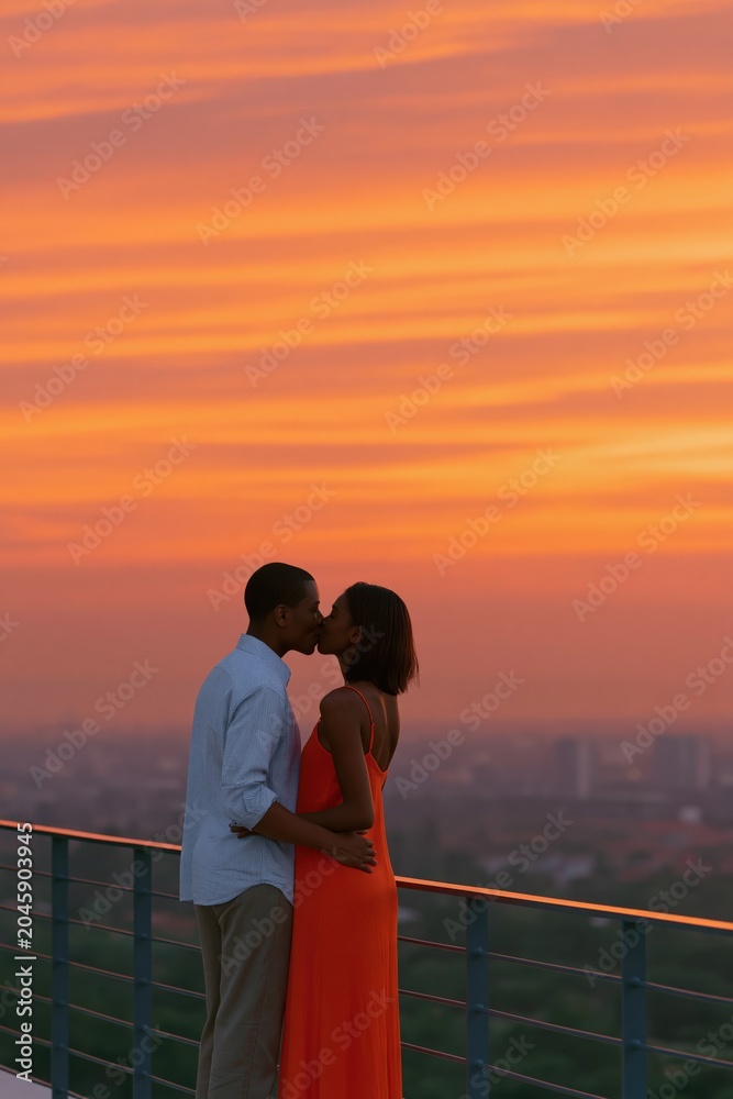 Fototapeta premium Rooftop couple kissing at vibrant orange sunset skyline background for romantic banner and lifestyle design