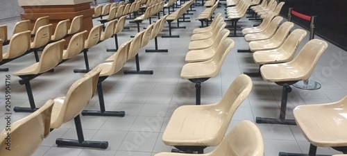 Schilderij op canvas A long row of empty metal and plastic chairs is arranged neatly along the wall of a brightly lit hospital waiting room hallway