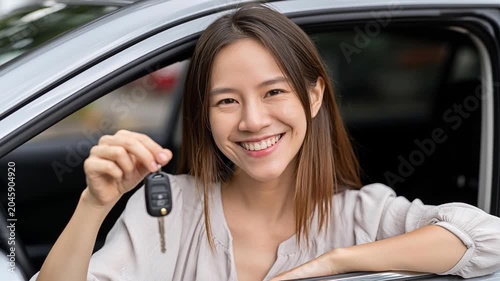 Joyful New Car Owner: A smiling young woman holds up car keys, sitting in the driver's seat of her new vehicle, radiating happiness and freedom.