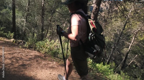 Woman hiking on a forest trail with backpack and trekking poles during an outdoor adventure