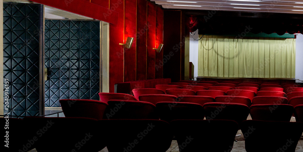 Fototapeta premium An empty theater with red velvet seats and a closed curtain awaits its next performance.