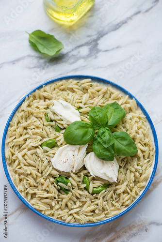 Orzo with basil oil, torn mozzarella cheese and fresh green basil, vertical shot on a white stone background, selective focus