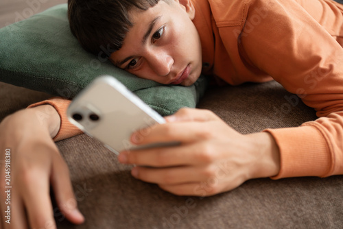 Fotografía Teenager lying on sofa staring at smartphone screen with absent expression