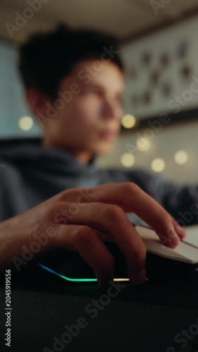 Close-up of a hand on a computer mouse with RGB lights. A teenage boy is playing a video game in his room at night. Vertical video.