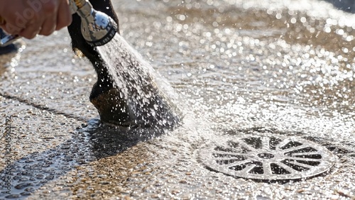 Water sprays from a hose onto a horse's hoof, creating splashes on a textured surface near a drain, showcasing the interaction between water and the animal's foot