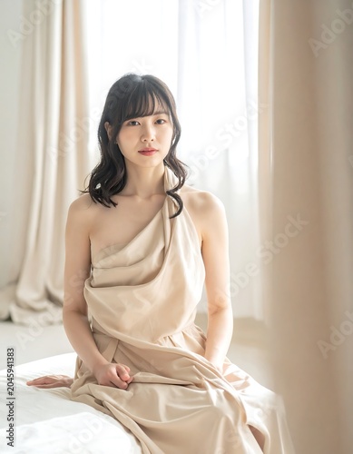 Woman draped in light fabric poses against a window