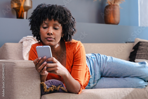 Individual browsing digital content, relaxing at home, holding wireless gadget, cheerful expression, cozy furniture, weekend leisure, online social communication, lifestyle, habit, hobby, activity