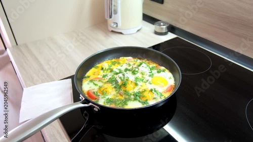 Cooking eggs with tomatoes and herbs on the stove in a frying pan at home in the morning