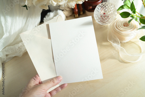 Mockup of a blank white card held by hand with soft blurred flowers, perfect for wedding or Valentine’s greeting design, with clipping path.