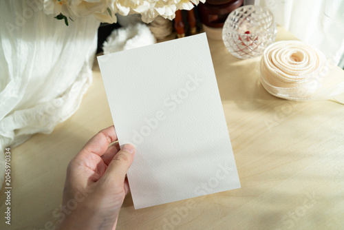 Mockup of a blank white card held by hand with soft blurred flowers, perfect for wedding or Valentine’s greeting design, with clipping path.