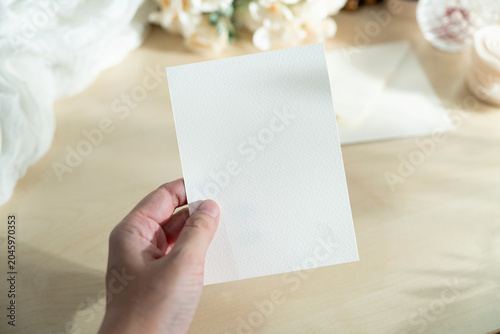 Mockup of a blank white card held by hand with soft blurred flowers, perfect for wedding or Valentine’s greeting design, with clipping path.