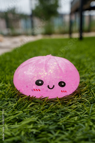Fotografie Cute pink glitter squishy toy resembling a smiling bun resting on green grass, p