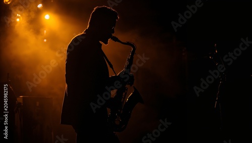 Silhouette of a man playing jazz saxophone with stage lighting in background