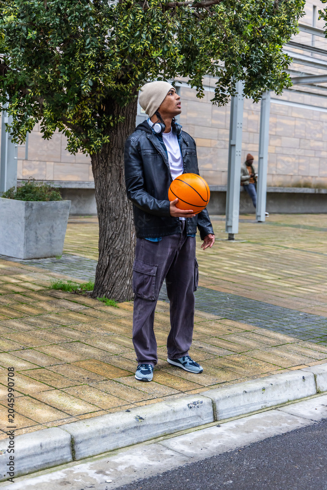 Fototapeta premium Diverse males standing, holding orange basketball, wearing beanie and headphones at plaza
