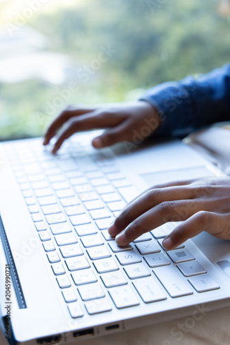 African American adult typing on white laptop keyboard with trackpad, USB-ports by window, in denim