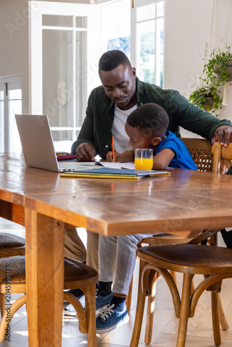 African American father and son studying at home table with laptop pencil and orange juice