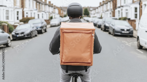 Urban delivery cyclist with insulated backpack navigates suburban street for contactless service