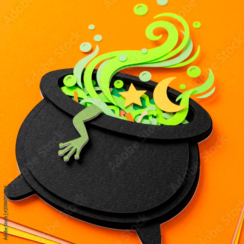A vibrant 3D paper Halloween witch's cauldron with a glowing frog paw containing a potion and magical sparks on a bright orange background [text space]