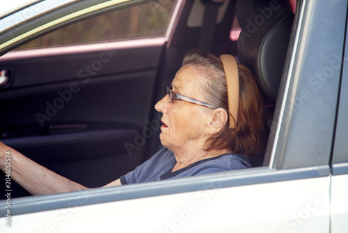 Old woman driving a car in the countryside, road trip concept.  Portrait of an old woman driving and near a car, on a walk outside the city.