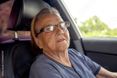 Old woman driving a car in the countryside, road trip concept.  Portrait of an old woman driving and near a car, on a walk outside the city.