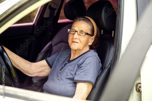 Old woman driving a car in the countryside, road trip concept.  Portrait of an old woman driving and near a car, on a walk outside the city.