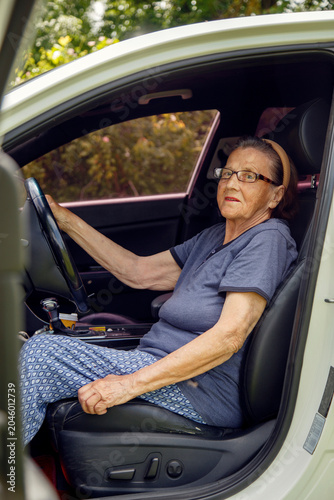 Old woman driving a car in the countryside, road trip concept.  Portrait of an old woman driving and near a car, on a walk outside the city.