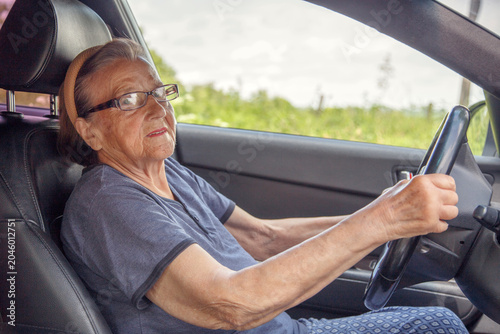 Old woman driving a car in the countryside, road trip concept.  Portrait of an old woman driving and near a car, on a walk outside the city.