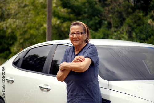 Old woman driving a car in the countryside, road trip concept.  Portrait of an old woman driving and near a car, on a walk outside the city.