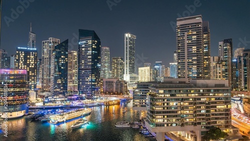 Stunning night view of Dubai's futuristic skyline with glowing towers, marina, and luxury boats along the waterfront.
