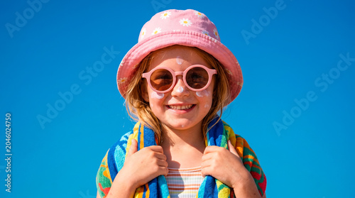 Smiling child with sunscreen on face wearing a pink hat and sunglasses