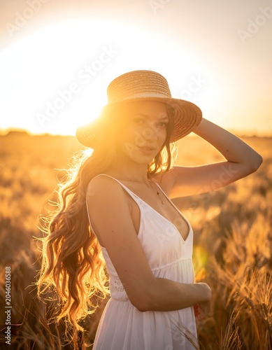 Woman in white dress, sunlit wheat field, wearing a hat. Long hair shines in golden light. Peaceful, serene scene