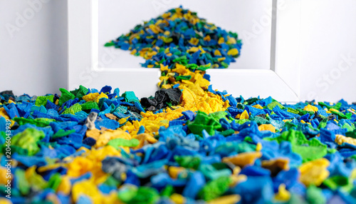 Abstract ecology banner with multi colored recycled polymer fragments arranged in a straight pathway on a white backdrop
