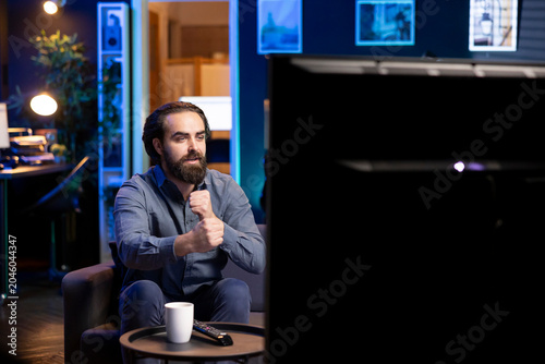 Fotografía Man relaxing at home on couch, being gripped by suspenseful films shown on television screen