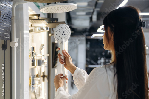 Fotografie Female technician inspecting modern showerhead in a contemporary bathroom showro