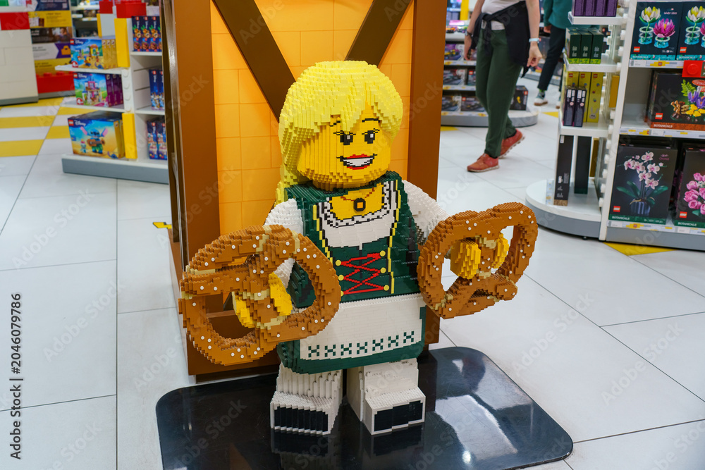 Naklejka premium Munich, Germany - May 31, 2026: LEGO figure in Bavarian costume holding giant pretzels inside a Munich store. Concept of local culture, tourism and creative design