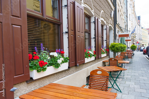 Slika na platnu Cozy outdoor cafe terrace with flower-filled window boxes along a historic Munic