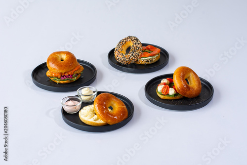 Variety of gourmet bagel sandwiches served on black plates over a white background.