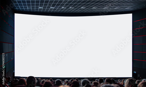 An audience sits in a dark cinema hall looking at a large blank white projection screen.