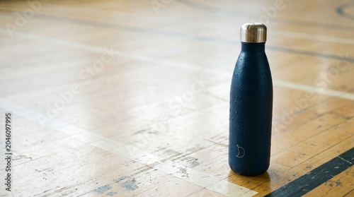Dark blue reusable water bottle with condensation on a wooden gym floor, hydration and fitness concept